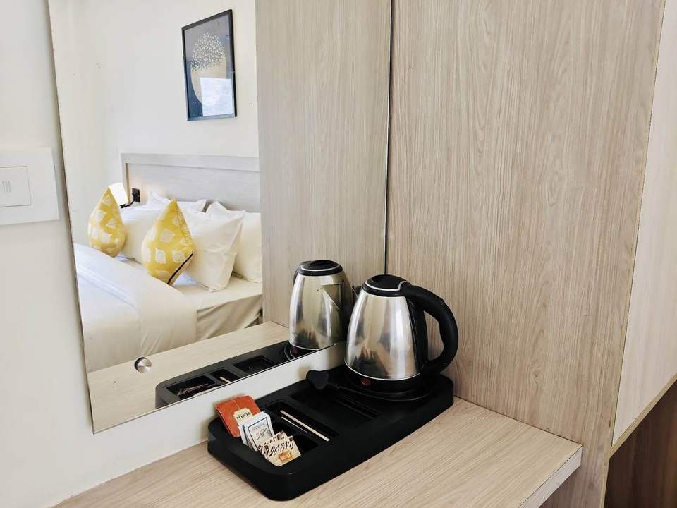 Two kettles and a tea tray beside a mirror reflecting the bed in a Deluxe Room at Alpine Retreat, Rishikesh