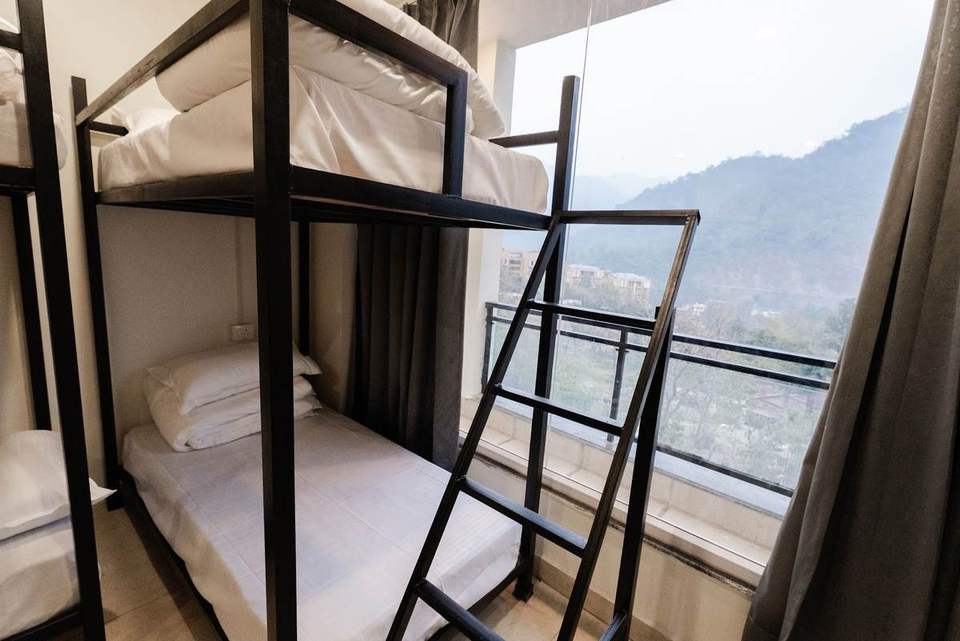 Six-bed dormitory with black metal bunk beds and a window facing the hills at Alpine Retreat, Tapovan, Rishikesh