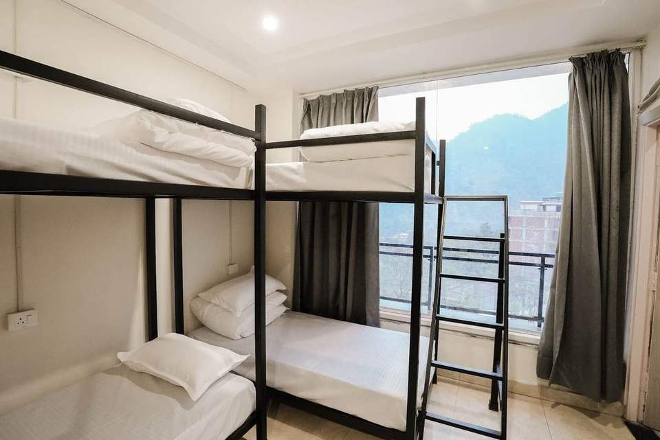 Bunk beds with fresh linen beside a large window with a mountain view in the Alpine Retreat dormitory, Rishikesh