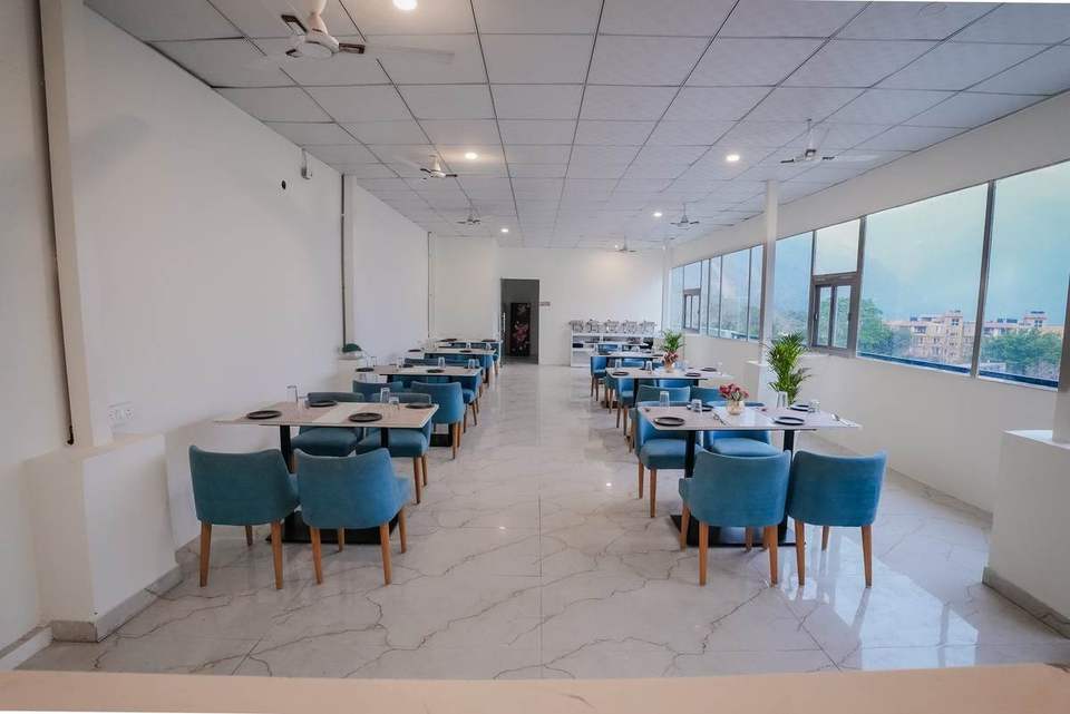 Long marble-floored dining hall with teal chairs and windows along one side at Alpine Retreat, Tapovan