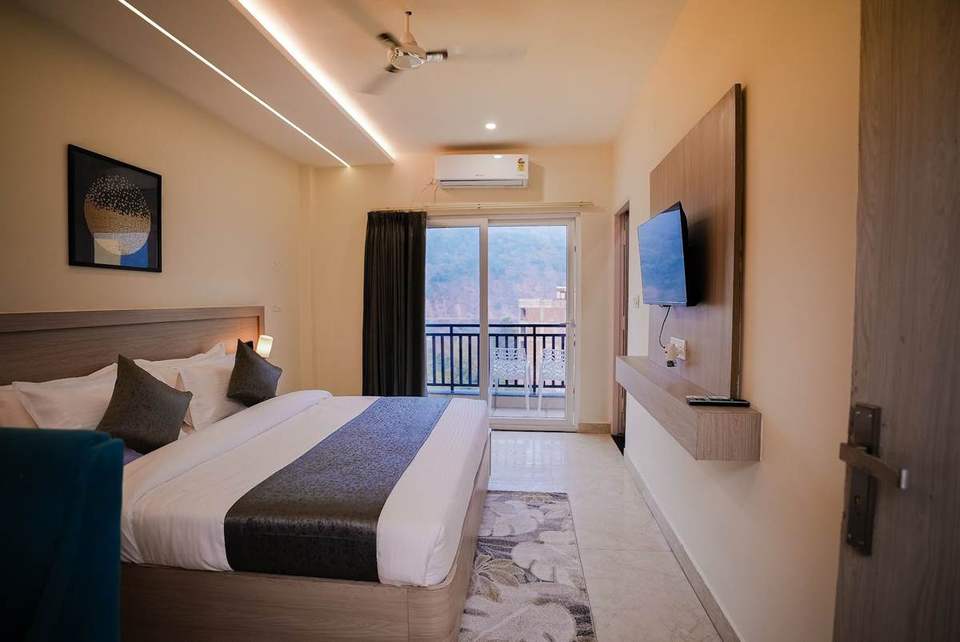 Standard Room with king bed, wall TV and balcony door at the far end at Alpine Retreat, Tapovan, Rishikesh