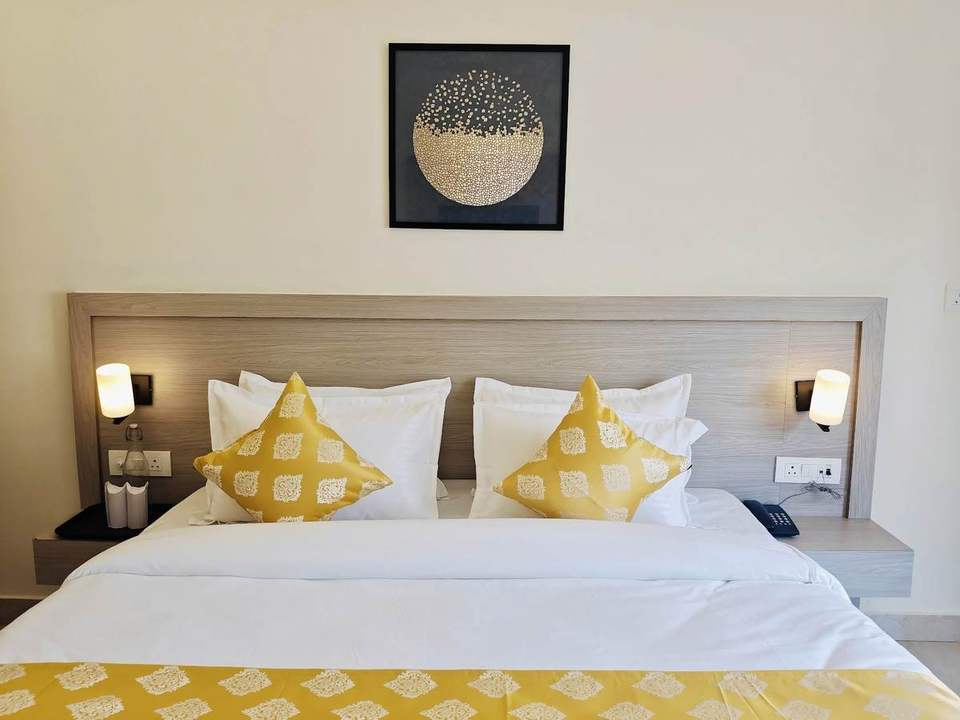 King bed with yellow patterned cushions and bedside lamps in a Super Deluxe Room at Alpine Retreat, Rishikesh