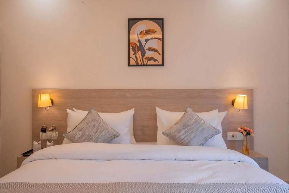 King bed with white linen and grey cushions between two wall lamps in a Super Deluxe Room at Alpine Retreat, Rishikesh