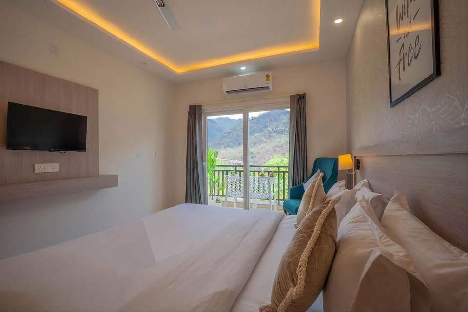 Super Deluxe Room bed with the balcony door open to green hills at Alpine Retreat, Rishikesh