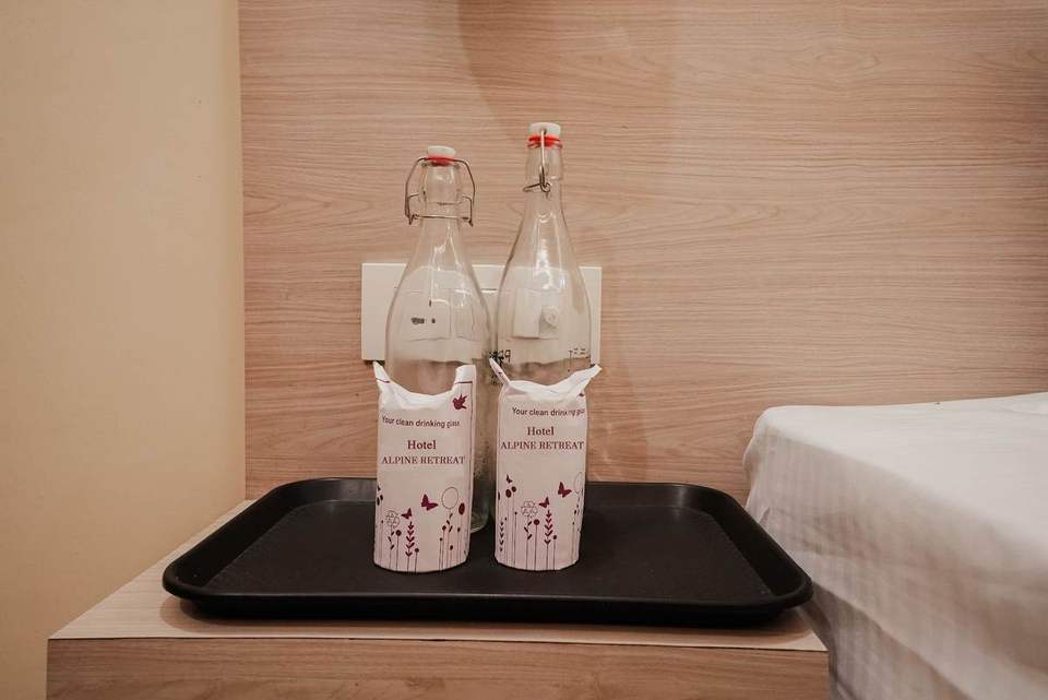 Two glass water bottles with Alpine Retreat labels on a bedside tray, Rishikesh